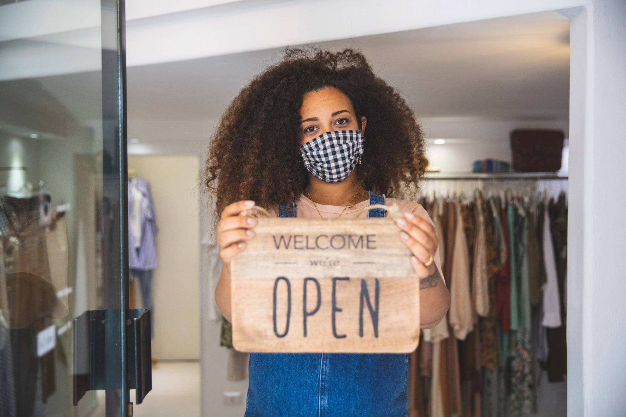 Woman holding Open sign in a small business boutique shop after Covid-19 pandemic Woman holding Open sign in a small business boutique shop after Covid-19 pandemic