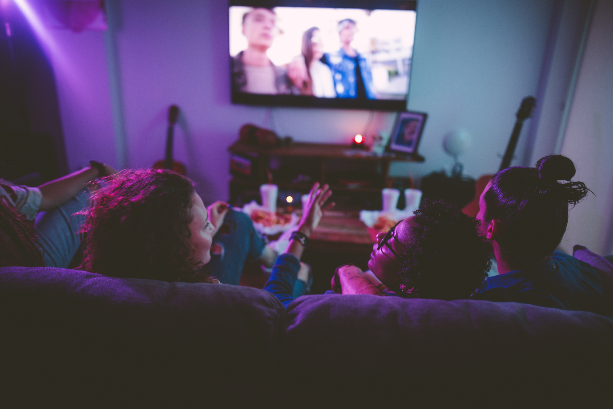 Multi-ethnic teenage friends watching TV together at hangout house